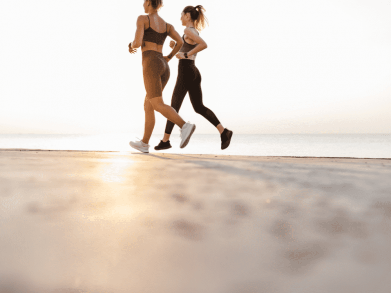Two women running on the beach as the sun rises